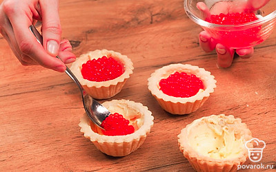 Заполните готовые тарталетки начинкой. При помощи маленькой ложки разложите размягченное сливочное масло по мини-корзиночкам. Сверху аккуратно распределите красную икру. Старайтесь, чтобы икринки легли на масло равномерно. Это придаст блюду аккуратный вид и выразительность.