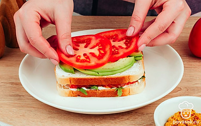 Накройте получившийся бутерброд вторым тостом, намажьте его сыром. Выложите на сыр авокадо, затем помидор.