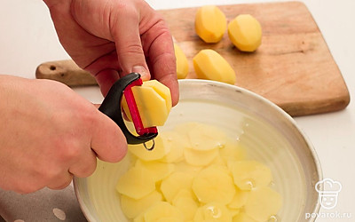 Нарежьте картофель слайсами и поместите в холодную воду на 3 минуты. Для нарезки картофеля используйте овощерезку. Затем слейте воду, выложите слайсы картофеля на бумажные полотенца и хорошенько просушите. Разогрейте духовку до 180°C.