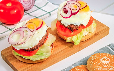 Сверху на котлеты выложите жареные яйца. Добавьте кольца красного лука.