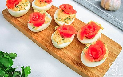 Яйца, фаршированные сёмгой выложите на большую плоскую тарелку. Украсьте блюдо помидорами черри и петрушкой.