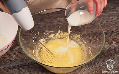 Начните готовить тесто. Для этого в глубокой миске миксером взбейте масло с сахаром и ванилином. Добавьте в тесто яйца, продолжая взбивать массу. Влейте молоко и перемешайте.