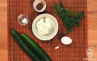 Подготовьте продукты для рулета. Огурцы вымойте, овощечисткой нарежьте тонкими продольными полосками. Яйцо отварите вкрутую, мелко нарежьте до состояния крошки. Измельчите чеснок. Для приготовления рулетов из огурцов в магазине можно купить уже готовый творожный сыр с зеленью.