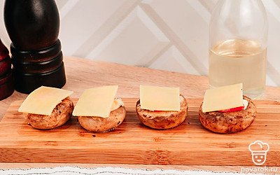 Накройте каждую шляпку ломтиком плавленного сыра и отправьте грибы в духовку на 10 минут при 180 °С.