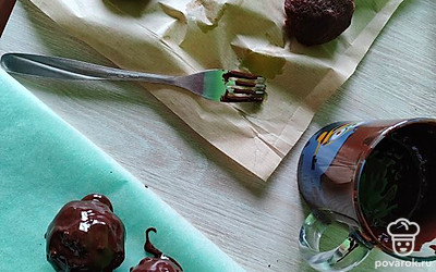 За 10 минут до готовности начинаем темперировать шоколад на водяной бане. У меня есть специальные дропсы, но можно использовать любой шоколад. Нагреваем на водяной бане с добавлением растительного масла. Для 100 граммов шоколада понадобится 1 чайная ложка масла. Переливаем шоколад в кружку, добавляем мелко нарезанные орешки. Втыкаем в картошку вилку, окунаем в шоколад и выкладываем на пергамент. Отправляем в морозилку на 15 минут. Оставляем одну столовую ложку шоколада и переливаем в кондитерский мешок. 