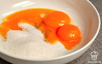 Сделайте заварную основу. К желткам добавьте сахар и взбивайте 30 секунд до однородной консистенции. Влейте молоко и вновь перемешайте. Влейте в другую кастрюлю стакан воды и доведите до кипения. Поставьте в эту кастрюлю посуду с заварной основой и варите ее на протяжении 10 минут, постоянно помешивая. Затем охладите посуду со смесью в холодной воде.