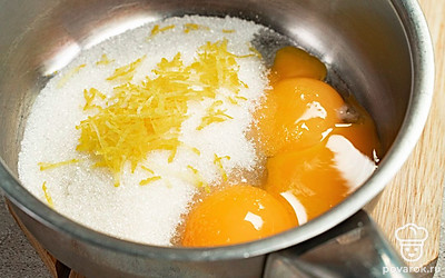 Приготовьте основу. Насыпьте в кастрюльку 100 г сахара, добавьте лимонную цедру, перетрите вилкой, чтобы цедра отдала вкус и аромат. Добавьте яичные желтки, молоко и перемешайте до гладкой однородной массы. Поставьте емкость на водяную баню и на медленном огне, помешивая, варите в течение 10 минут, пока масса не загустеет. Остудите, влейте лимонный сок, перемешайте.