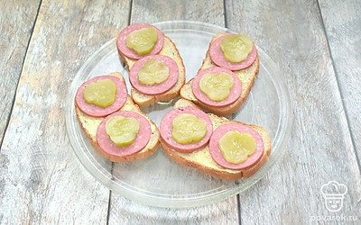 Соленый или маринованный огурец нарежьте тонкими колечками. Выложите колечки огурца на колбасу.