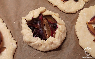 Присыпьте сливу сахаром и заверните края, чтобы начинка при выпекании не вытекала. У меня в морозилке нашлась горсть замороженных ягод черники, я добавила по несколько штучек в каждую заготовку. 