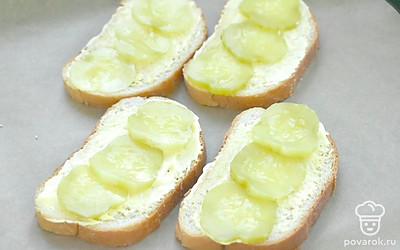 Соленый огурец нарежьте колечками. Выложите по 2-3 штуки на каждый ломтик батона. 
