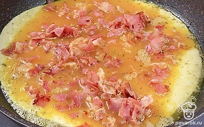 Формируем пирог. Для этого в сковороду высыпаем семена кунжута, выкладываем лепешку и поверх поливаем яичной смесью. Посыпаем обжаренным беконом, выкладываем тертый сыр и накрываем второй лепешкой. Жарим под крышкой на среднем огне 10 минут, пока яйца не схватятся.