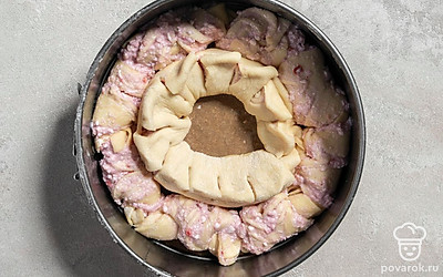 Оставшееся тесто разделите на 2 части. Одну часть раскатайте в тонкий прямоугольник и смажьте его начинкой, скрутите в рулет и присыпьте манкой. Сделайте на рулете надрезы и выложите внутрь формы, разворачивая лепестки кверху.