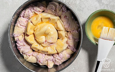 Оставшееся тесто раскатайте в тонкий пласт, смажьте начинкой и так же сверните в рулет. Этот рулет скрутите жгутом и положите в центр формы. Смажьте пирог желтком и отправьте в разогретую до 180°C духовку на 25 минут.