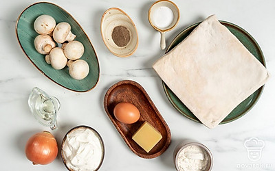 Помойте и промокните бумажным полотенцем шампиньоны и яйцо. Вымойте и почистите лук. Разморозьте тесто по инструкции на упаковке. Подготовьте сковороду, скалку, миску, терку, противень и блюдо для подачи. Смажьте противень 1 ч. л. подсолнечного масла.