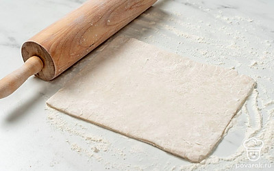 Припылите стол оставшейся мукой, разложите на нем слоеное тесто. Раскатайте его до толщины 4-5 мм.