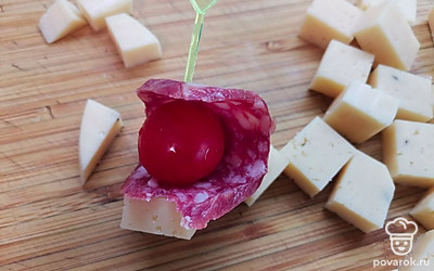 Чери оберните кусочком колбасы. Нанижите на шпажку и добавьте кусочек сыра. 
