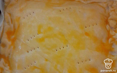 В форму для запекания выкладываем лист пергамента, на него кладем половину упаковки бездрожжевого готового теста, делаем небольшие бортики и выливаем нашу начинку. Сверху закрываем второй частью теста, края скрепляем между собой, чтобы начинка не вытекла. Делаем проколы вилкой и смазываем яйцом.