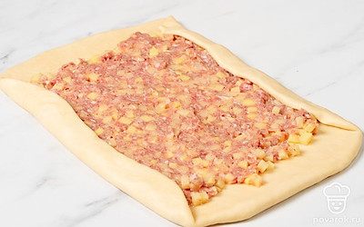 Разложите на тесто начинку и разровняйте ее. Когда будете раскладывать начинку, отступайте от краев теста по 1,5-2 см. Подогните эти края так, чтобы они легли на начинку. После этого сверните тесто в рулет.