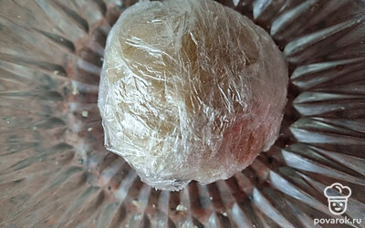 Влить в тесто 100 миллилитров холодной воды ложкой. Сделать вот такой колобок и завернуть его в пищевую пленку. Убрать в холодильник примерно на 1 час, чтобы масло в тесте успело замерзнуть.