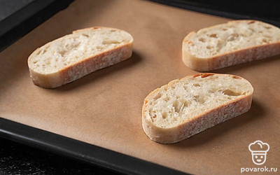 Положите ломтики багета на застеленный пергаментом противень и отправьте в разогретую до 200 ˚C духовку на 5 минут.
