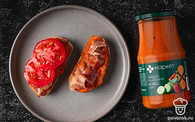 Каждый ломтик багета смажьте 1 ст.л. кабачковой икры. Сверху выложите по 1-2 полоске бекона, сложенной гармошкой. На бекон положите 1 или 2 кружочка помидора.