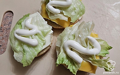 Накройте котлеты плавленым сыром. Выложите листья салата и смажьте майонезом. 