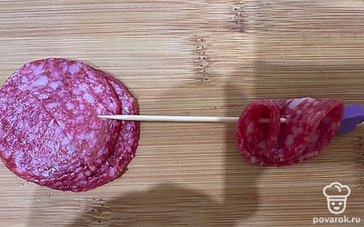 Сырокопченую колбасу, нарезанную тонкими слайсами, сверните и наденьте на шпажку.