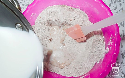 Приготовьте тесто для коржей, для этого в глубокой миске соедините ранее просеянную муку, разрыхлитель, сахар и какао-порошок. Перемешайте сухие ингредиенты и влейте к ним теплое молоко. Тщательно перемешайте мучную смесь до получения гладкой и однородной консистенции.