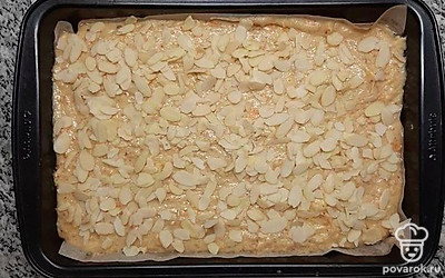 Возьмите прямоугольную форму размером примерно 30х18 см. Смажьте растительным маслом и постелите пергамент, чтобы потом пирог было легко достать из формы. Выложите полученное тесто в форму, разровняйте лопаткой и посыпьте миндальными пластинками. Поставьте выпекаться в разогретую духовку до 180°С на 30 минут. После приготовления пирог оставьте в форме еще минут на 15, затем достаньте и остудите.