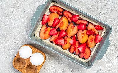 Сформируйте пирог. Тесто разделите на две части, одна должна быть больше другой. Большей частью выложите дно формы, формируя невысокие бортики. Распределите по тесту сливы и клубнику.