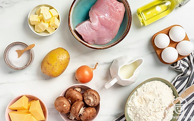 Помойте и обсушите яйца, отделите желток от белка. Просейте муку. Разморозьте, промойте и обсушите филе индейки. Помойте и промокните полотенцем шампиньоны. Почистите, помойте и обсушите картофель и лук. Порежьте филе на кубики, грибы на пластинки, картошку на кружочки, а луковицу на полукольца. Заранее достаньте сливки из холодильника. Натрите сыр. Подготовьте пищевую пленку.