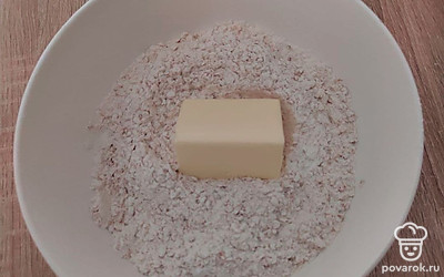 В удобную емкость поместите 70 г сахара, муку, хлопья и разрыхлитель. Тщательно перемешайте все ингредиенты. Туда же отправьте 100 г масла, и перетрите руками.