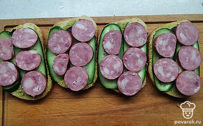Краковскую колбасу почистите, нарежьте кружочками и выложите на огурцы. 