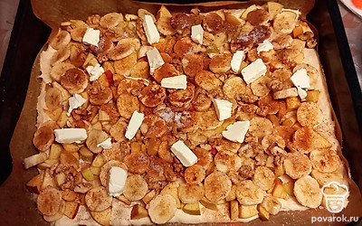 Нарежьте яблоки, бананы и грецкий орех кусочками. Выложите равномерно нарезанные яблоки, бананы, грецкий орех на тесто. Равномерно посыпьте выложенные на тесто нарезанные яблоки, бананы, грецкий орех сахаром и корицей. Сливочное масло нарежьте маленькими кусочками и выложите сверху на пирог.