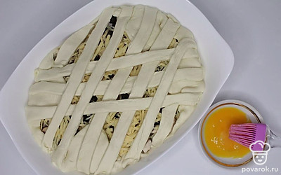 Тесто разделите на две части. Одну часть раскатайте толщиной 1 см и переложите в форму для запекания, смазанную маслом, наколите вилкой, чтоб в процессе выпечки не образовывались пузыри. Сверху ровным слоем положите куриное филе с шампиньонами, сверху сыр и маслины. Раскатайте второй слой теста, разрежьте на полоски шириной 1,5 см и уложите, переплетая их между собой, поверх начинки, формируя решетку. Оставьте пирог на расслойку на 15 – 20 минут. Смажьте сверху взбитыми яйцами, посыпьте кунжутом и семенами льна. Выпекайте в разогретой духовке при температуре 180 °C 40 минут.