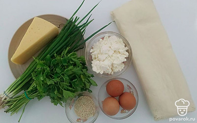Отварите вкрутую яйца, очистите их и нарежьте. Сыр натрите на терке. Измельчите зелень. Тесто разморозьте при комнатной температуре и разделите на две равные части. Раскатайте из них прямоугольные части.