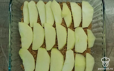 Измельчите орехи (ножом, скалкой или в комбайне) и смешайте с половиной сахара. Высыпьте на дно формы, разложите сверху одно яблоко, нарезанное дольками.