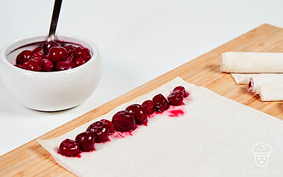 Подготовьте рулеты из фило с вишней. На столе, доске или коврике для раскатки теста разложите пласт фило. На нижний край выложите ягоды длинным, ровным рядом. Сверните в рулет. То же самое проделайте с остальными листами теста и вишней.