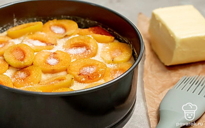 Приготовьте пирог с абрикосами. Форму для запекания смажьте маслом и присыпьте мукой или застелите пергаментом. Выложите тесто. Распределите равномерно по поверхности абрикосы внутренней стороной вверх. Сверху каждую дольку присыпьте оставшимся сахаром (50 г). Запекайте при 180 градусах 40-50 минут.