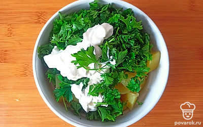 Выложите приготовленный картофель и петрушку в глубокую посуду. Добавьте сметану и измельчите толкушкой в пюре.