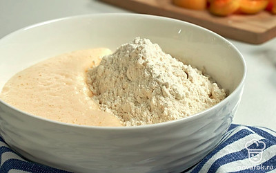 Добавьте муку и вымесите тесто. В яичную смесь постепенно просеивайте муку через сито. Каждый раз размешивайте тесто лопаткой или ложкой. После добавьте нарезанные абрикосы в тесто и аккуратно размешайте лопаткой.