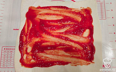 Раскатайте слоеное тесто толщиной 5-7 миллиметров. Обильно смажьте поверхность любым кетчупом. Верх теста не смазывайте. 