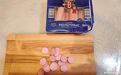Возьмите 2 молочных сосиски, очистите от целлофана. Нарежьте тонкими кольцами. 
