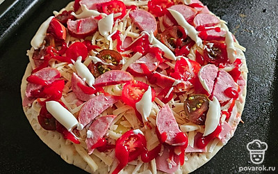 Сыр разделите на две части. Одну часть выложите на основу, затем распределите помидоры и колбасу. Для того, чтобы пицца получилась сочной, еще раз добавьте кетчуп и майонез. 