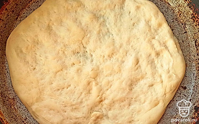 Посыпаем поверхность манкой, чтобы тесто не прилипало. Аккуратно руками раскатываем тесто. Смазываем соусом. Выкладываем любую начинку.