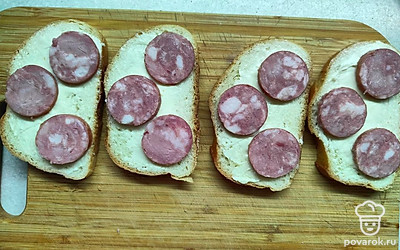 Колбасу нарежьте кружочками, предварительно сняв шкурку. Ломтики хлеба слегка смажьте сливочным маслом. Выложите колбасу на бутерброды. 
