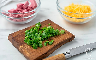 Пока печется основа для пиццы, натрите сыр и нарежьте колбасу маленькими кубиками. Измельчите зеленый лук.