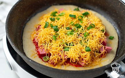 Когда лепешка из теста схватится и перестанет быть жидкой сверху, аккуратно переверните ее на другую сторону. Смажьте кетчупом. Равномерно выложите сверху колбасу, посыпьте сыром и луком, отступая от края по 1 см. Накройте крышкой, уменьшите нагрев до минимального. Готовьте еще 3 минуты.