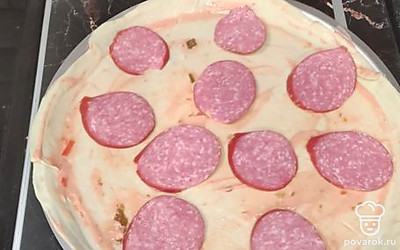 Далее форму немного смазать подсолнечным маслом, сверху положить тесто. Тесто смазать смесью из кетчупа и майонеза, сверху выложить нарезанную колбасу. 