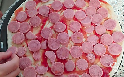 Порежьте сосиски на круглишки и равномерно разложить на смазанную соусом основу для пиццы.